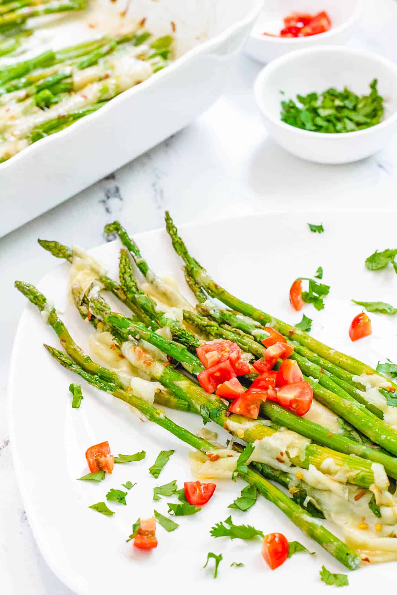 one serving of easy cheesy baked asparagus recipe with mozzarella, parmesan and tomatoes on a white plate