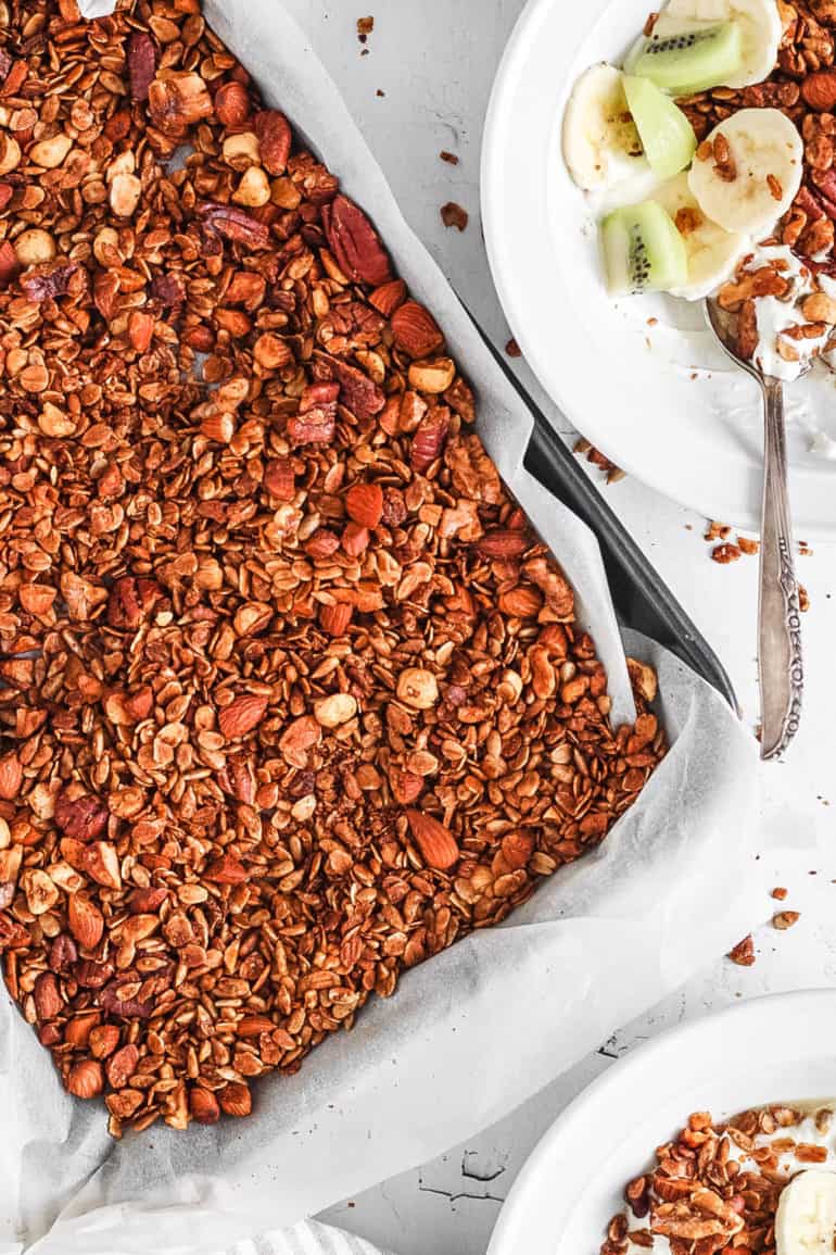 A baking pan of high protein granola with sliced fruit and a spoon.