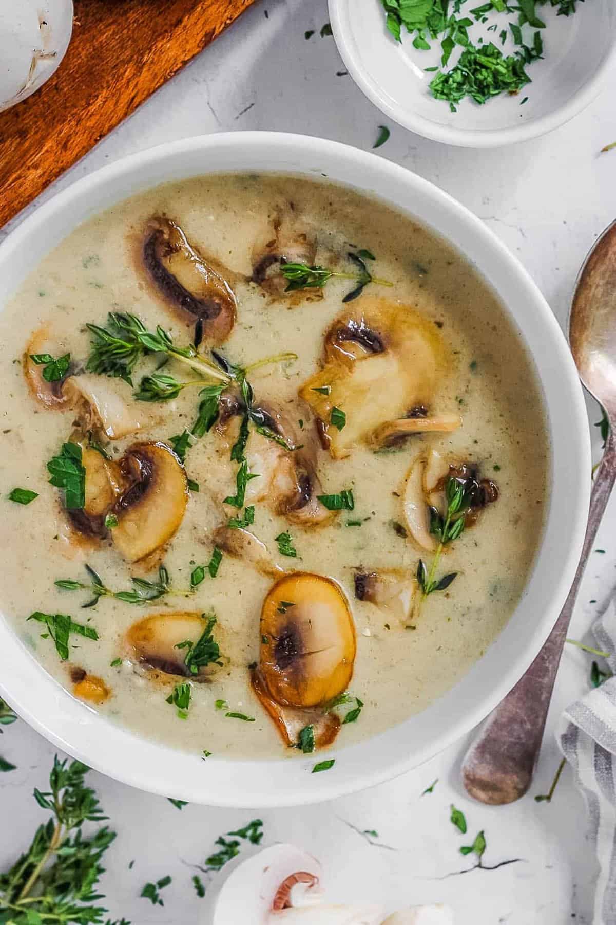 Healthy mushroom soup without cream in a white bowl, garnished with fresh herbs.