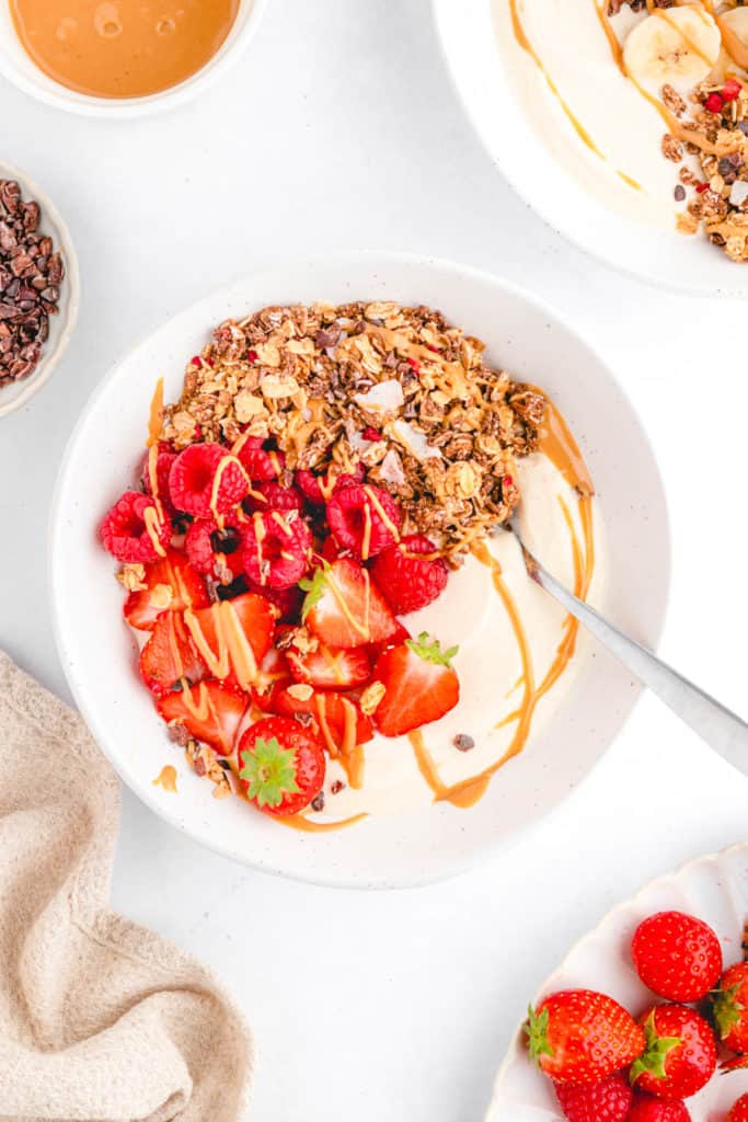 Overhead shot of a white bowl of a peanut butter bowl topped with peanut butter, berries, and granola.