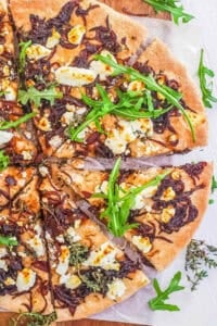 Goat cheese and caramelized onion pizza cut into slices on a white cutting board.