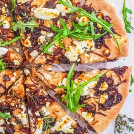 Goat cheese and caramelized onion pizza cut into slices on a white cutting board.