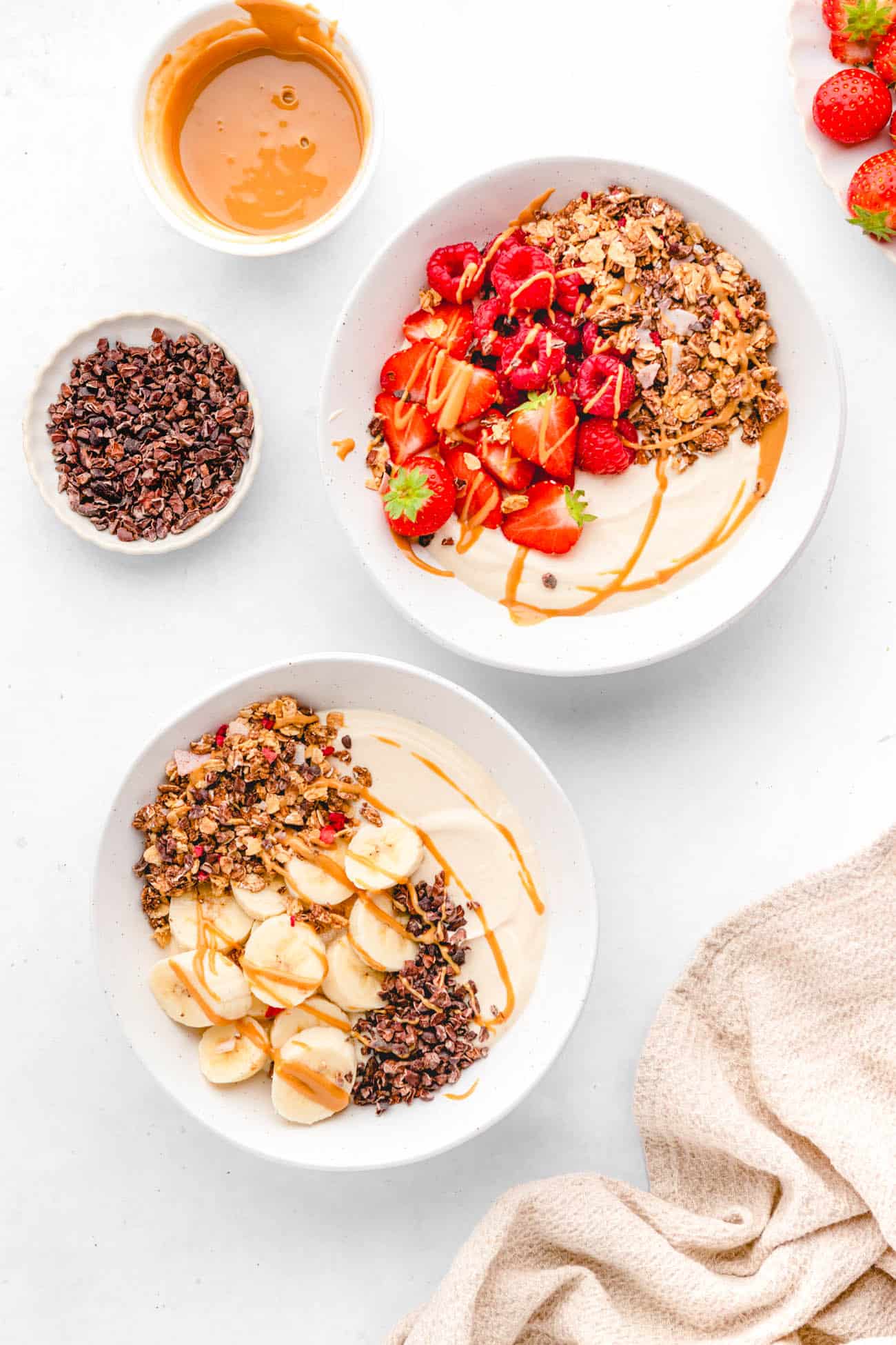 healthy yogurt bowl recipe topped with berries and granola in a white bowl and banana cacao as well