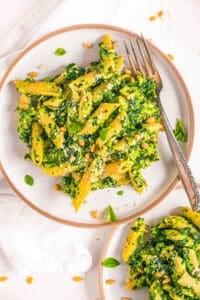 Vegetarian pesto pasta recipe with spinach, basil and pine nuts on a white plate.