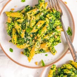 Vegetarian pesto pasta recipe with spinach, basil and pine nuts on a white plate.