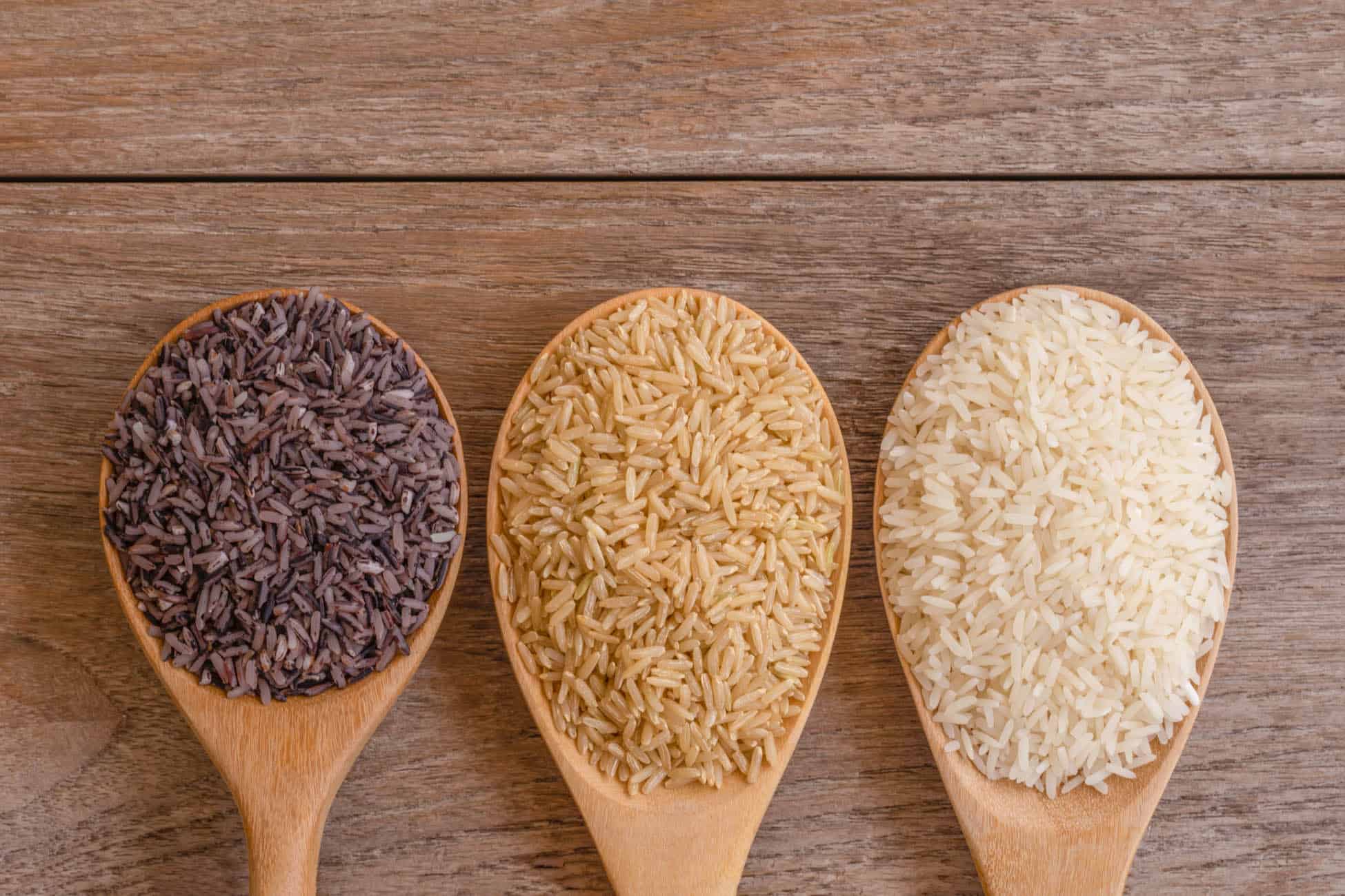 Variety type and color of rice ; paddy rice, riceberry ,brown coarse rice and white thai jasmine rice in wooden spoon isolated on old rustic wood table background. Healthy food concept. Flat lay.