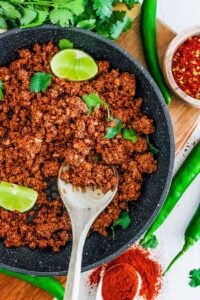 An overhead shot of a grey skillet of vegan chorizo with a wooden spoon.