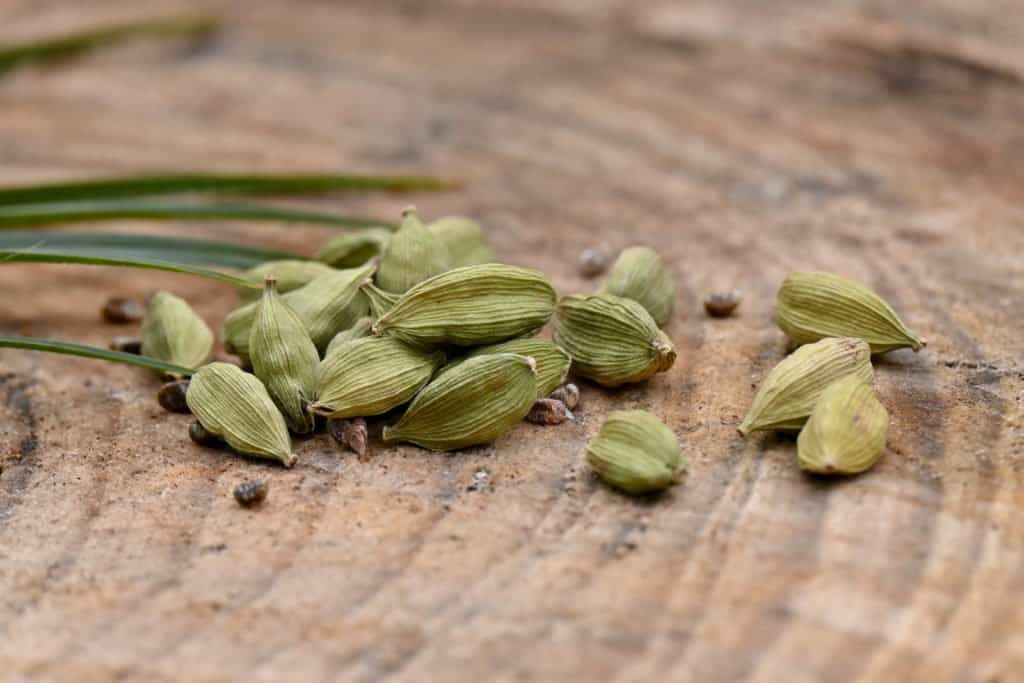 closeup of a bunch green ripe cardamom with green leaves over out of focus wooden background - best substitute for cardamom