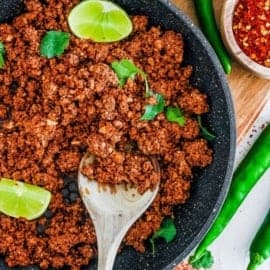 An overhead shot of a grey skillet of vegan chorizo with a wooden spoon.