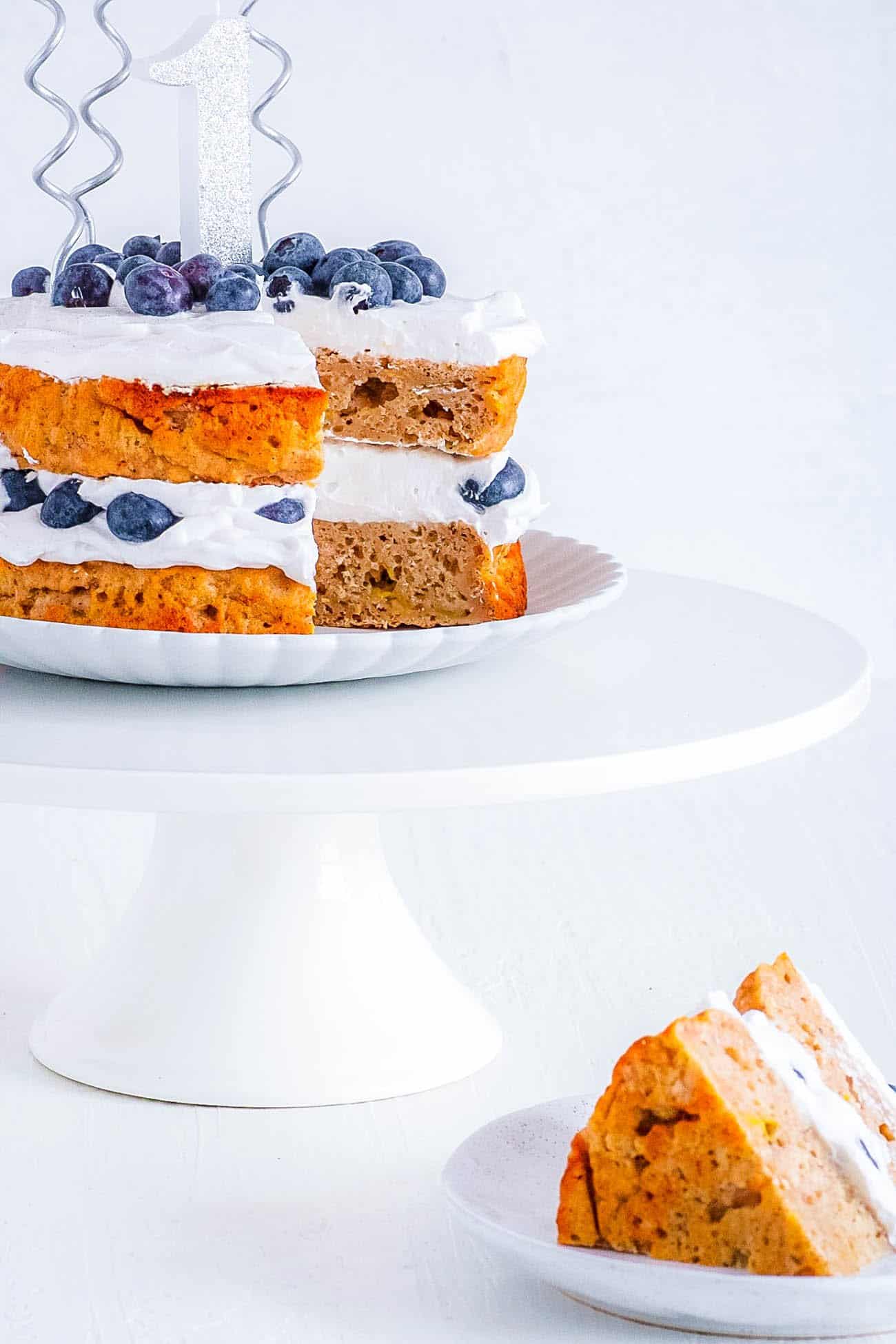 Healthy smash cake with a piece cut out of it and the piece on a white plate in the foreground.