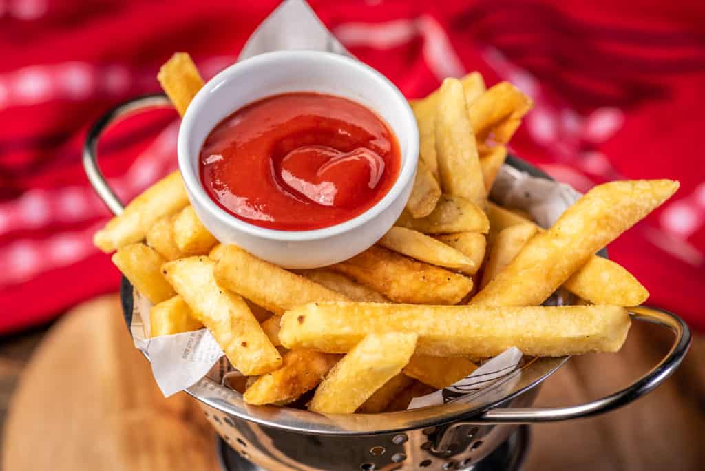 Golden French Fries in a metal colander with Tomato Sauce in a small white bowl