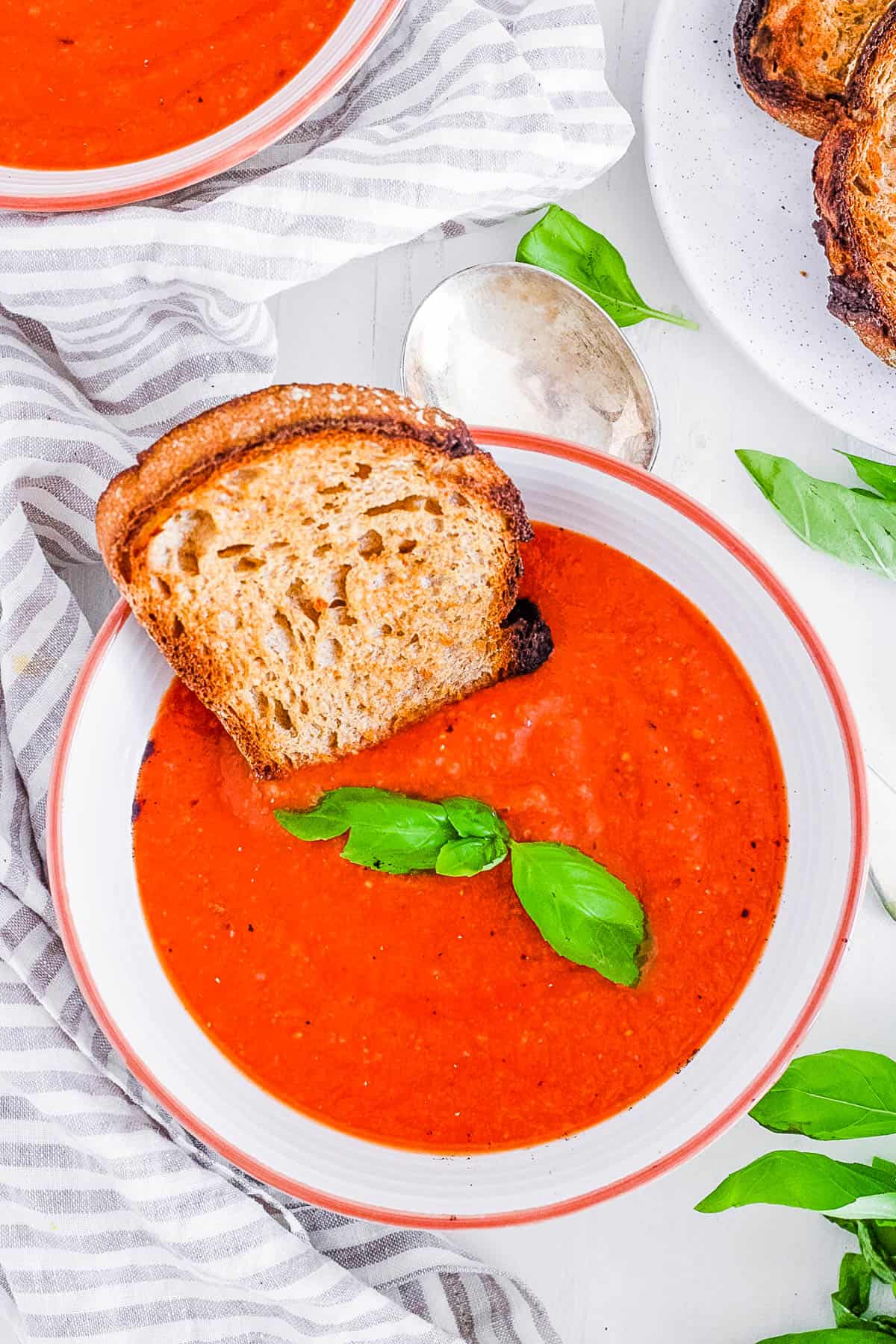 An overhead shot of a white bowl of tomato soup with toast.