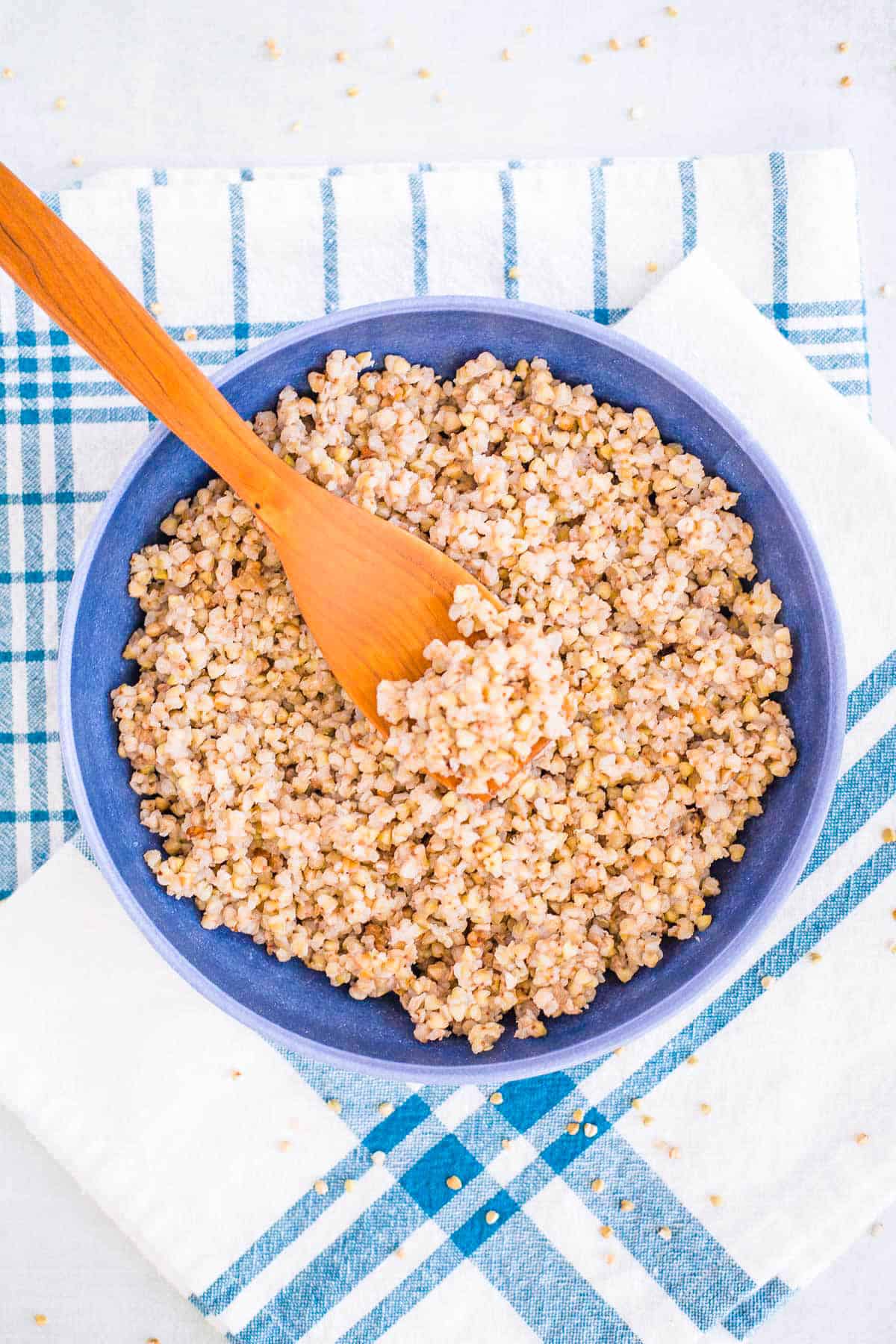 An overhead shot of a blue bowl of buckwheat on a striped blue towel.