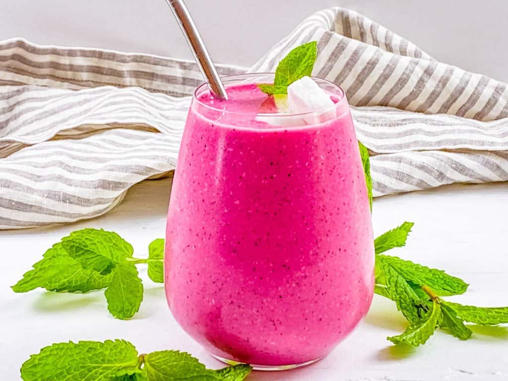 A glass of dragonfruit smoothie on a counter with a napkin.