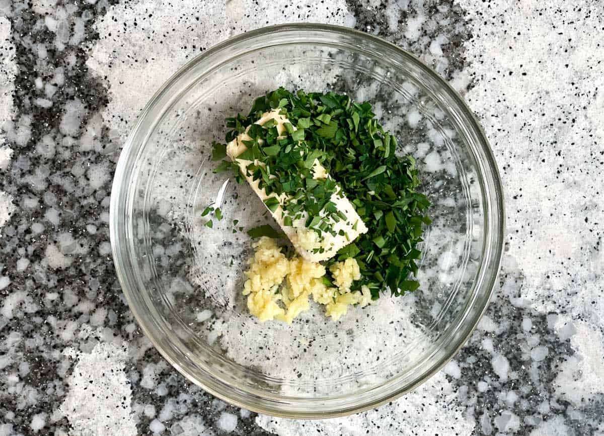 Butter, parsley, salt, and minced garlic in glass bowl.