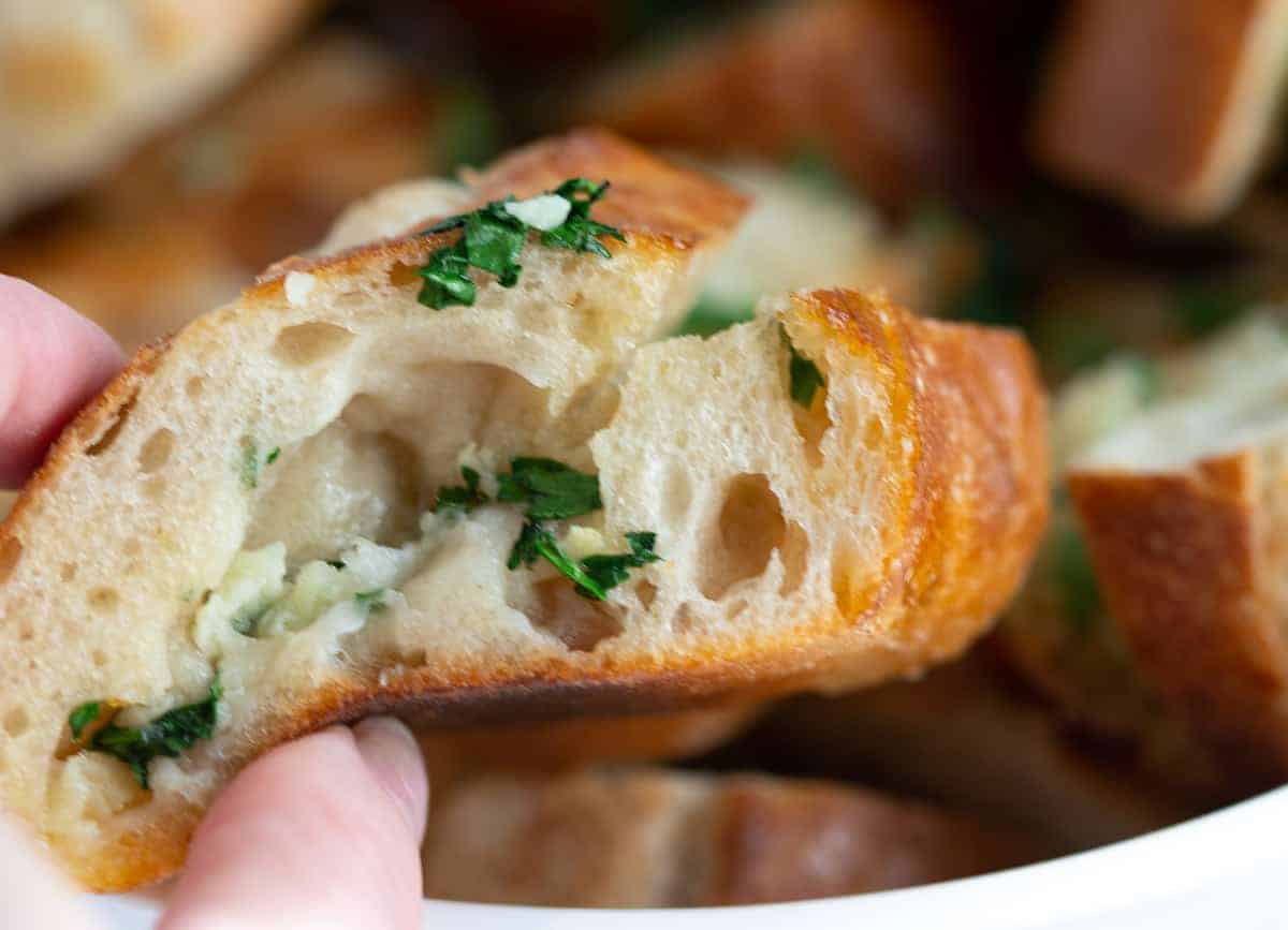 Hand holding slice of garlic bread.