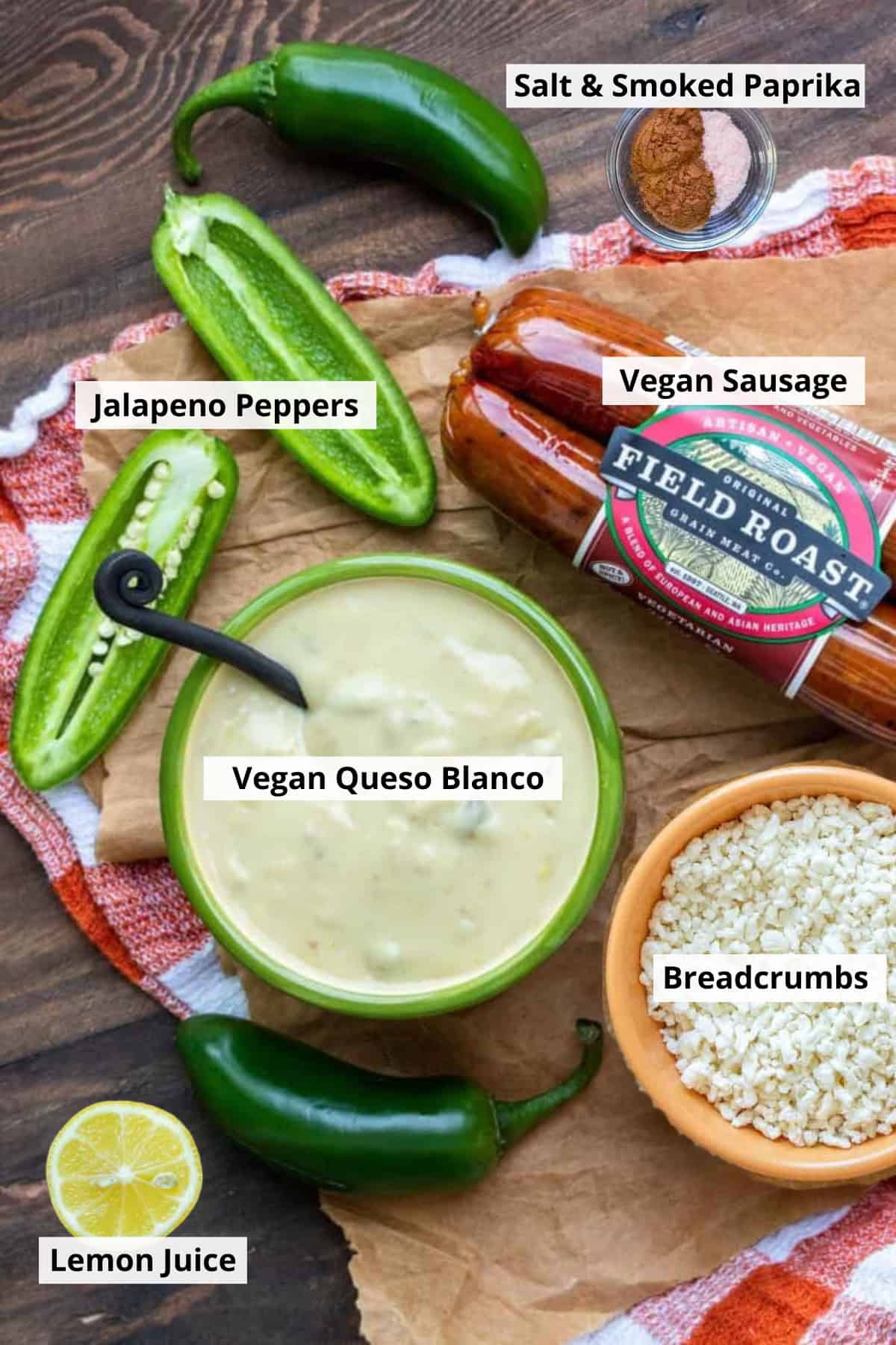 Ingredients for vegan jalapeno poppers recipe: vegan sausages, jalapeños, breadcrumbs, and bowl of vegan white cheese sauce -- on a wood counter top. 