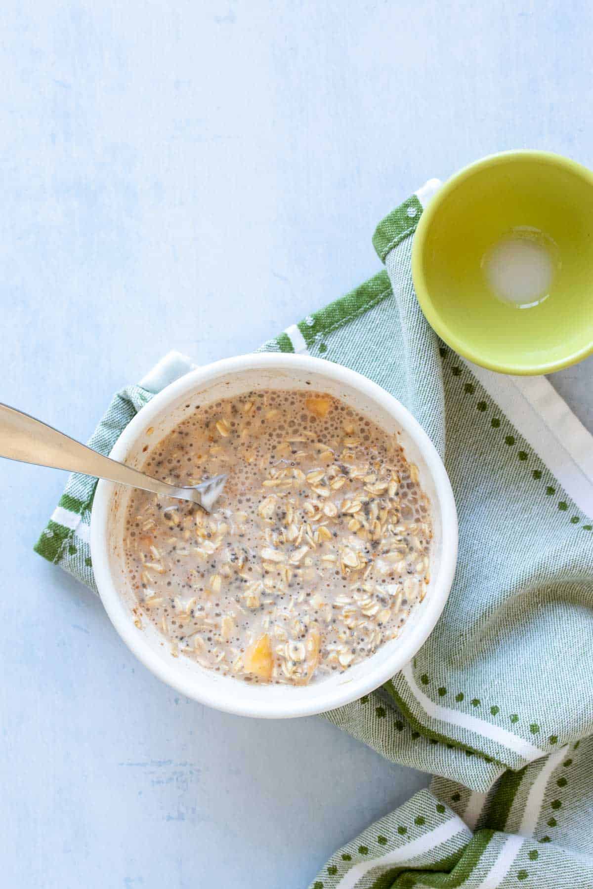 A spoon mixing oats, milk, peaches and other ingredients in a white bowl
