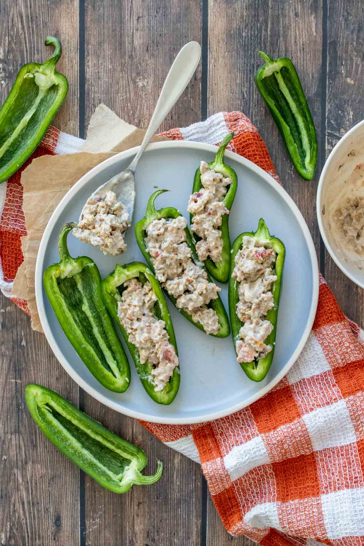 A grey plate with halved jalapenos stuffed with a sausage and cream mixture on a checkered towel.