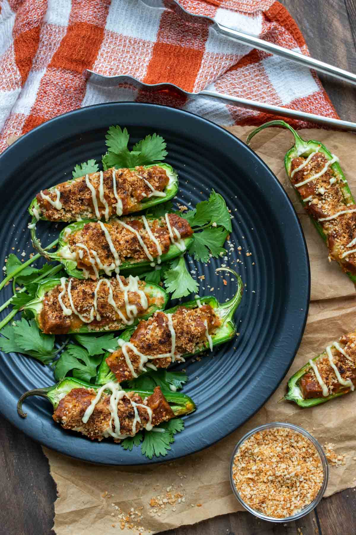 Top view of vegan stuffed jalapeños drizzled with white cheese sauce on a black plate.