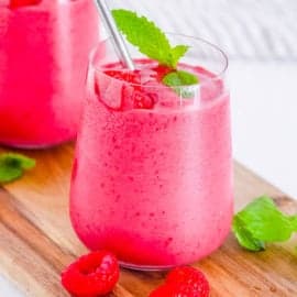 Two glasses of raspberry smoothie with mint on a wooden cutting board.