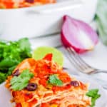 slice of easy healthy vegetarian layered taco casserole with tortillas, white baking dish in the background