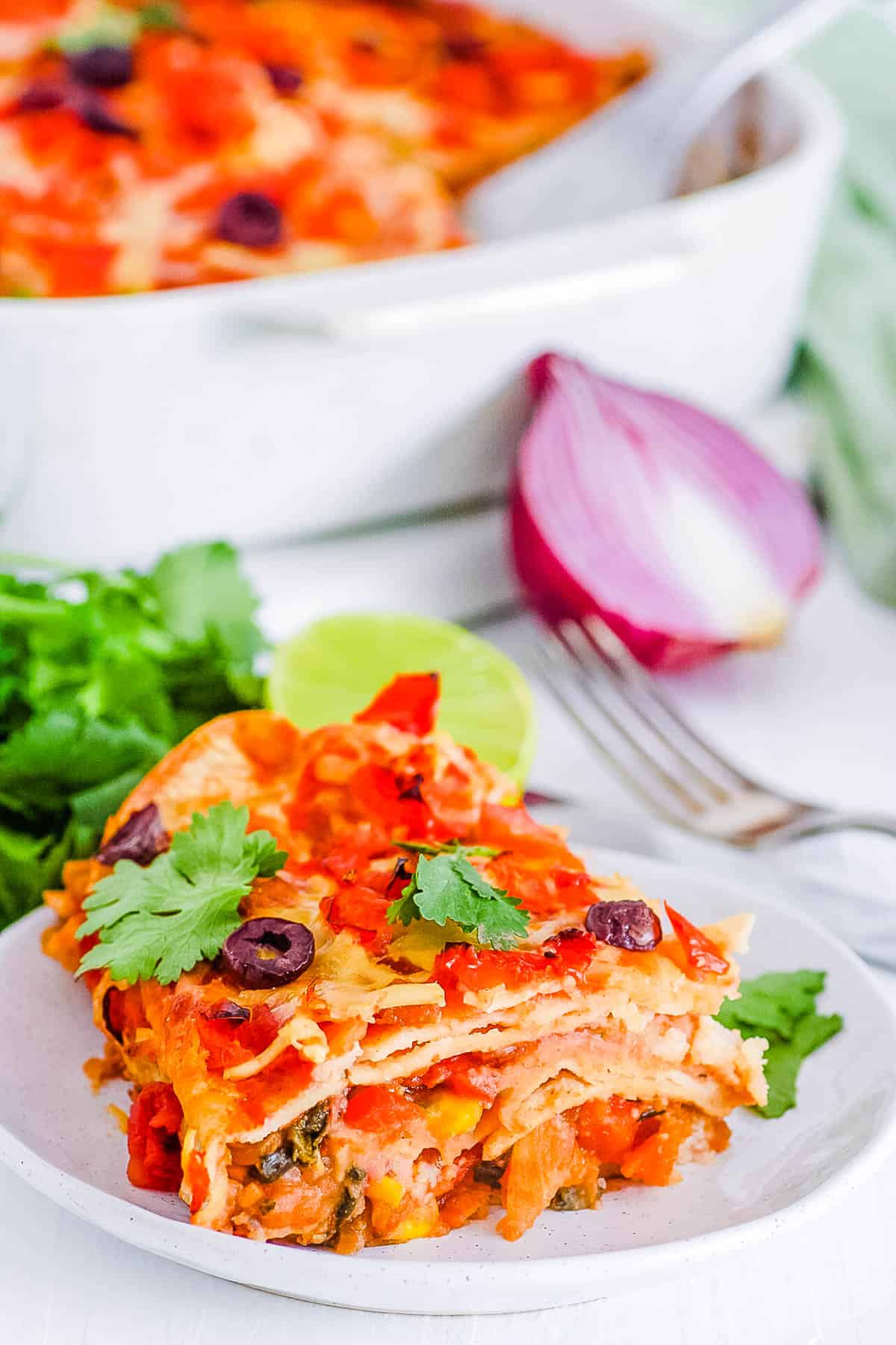 slice of easy healthy vegetarian layered taco casserole with tortillas, white baking dish in the background