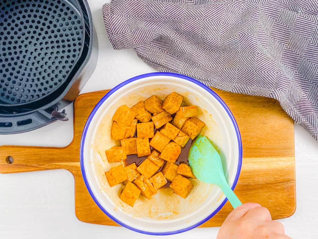 Turning the tempeh cubes in the marinade in the mixing bowl.