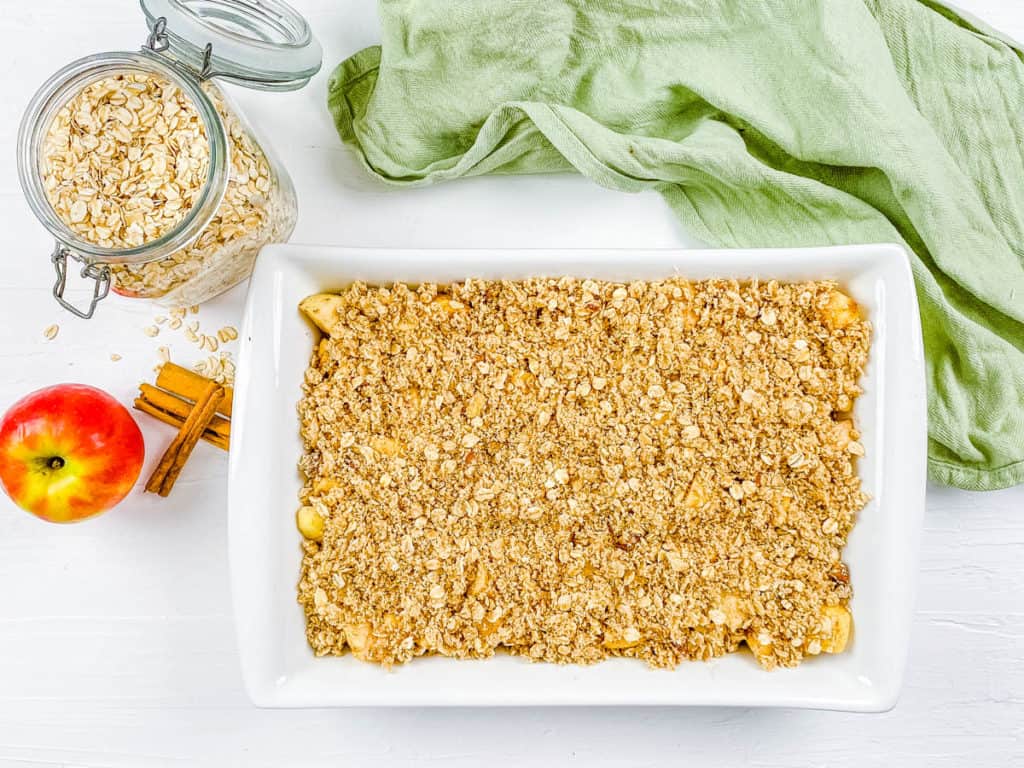 topping added to apple crisp in a baking dish