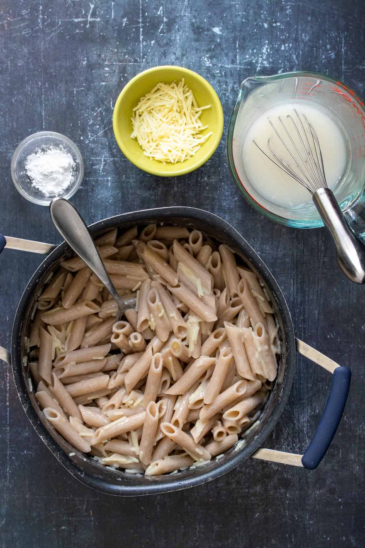 Top view of pasta mixed with parmesan in a pot next to bowls with tapioca starch, Parmesan and pasta water