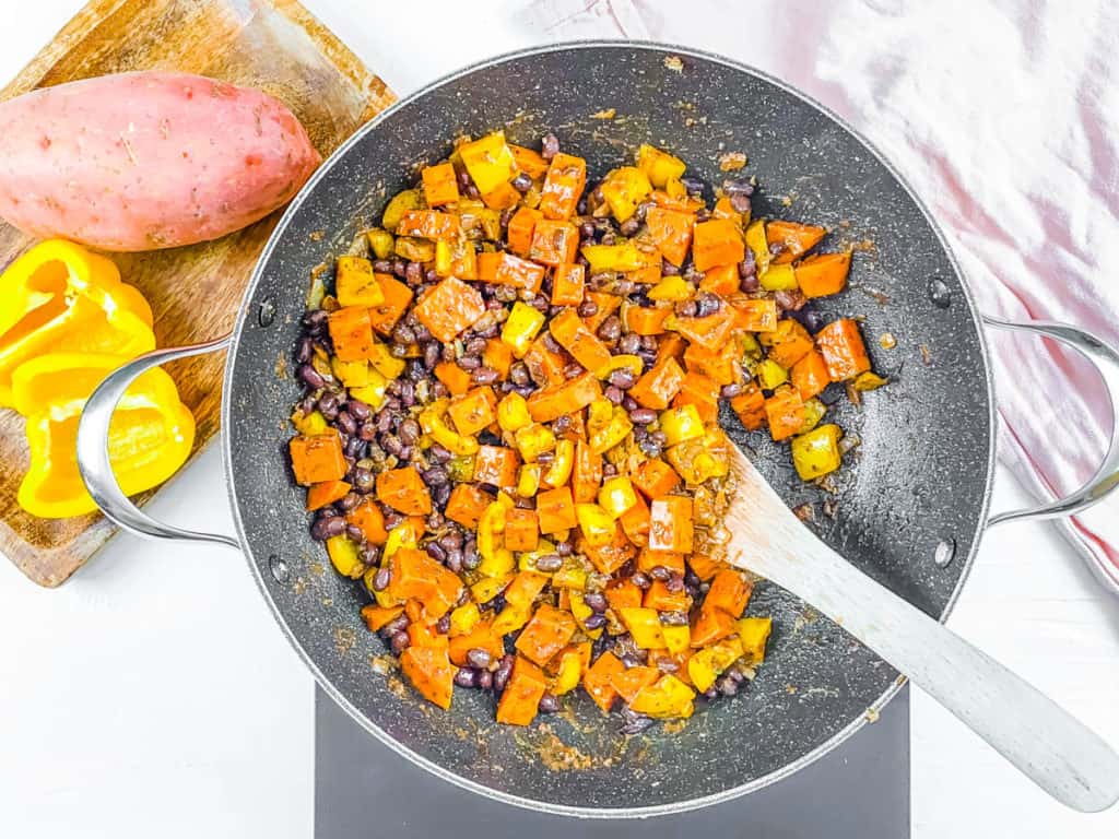 Seasoned black beans, peppers, and sweet potatoes cooking in a wok. 