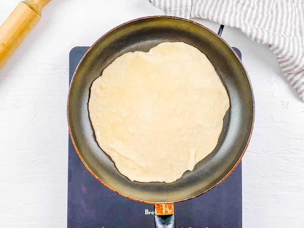 paratha dough in a skillet being cooked