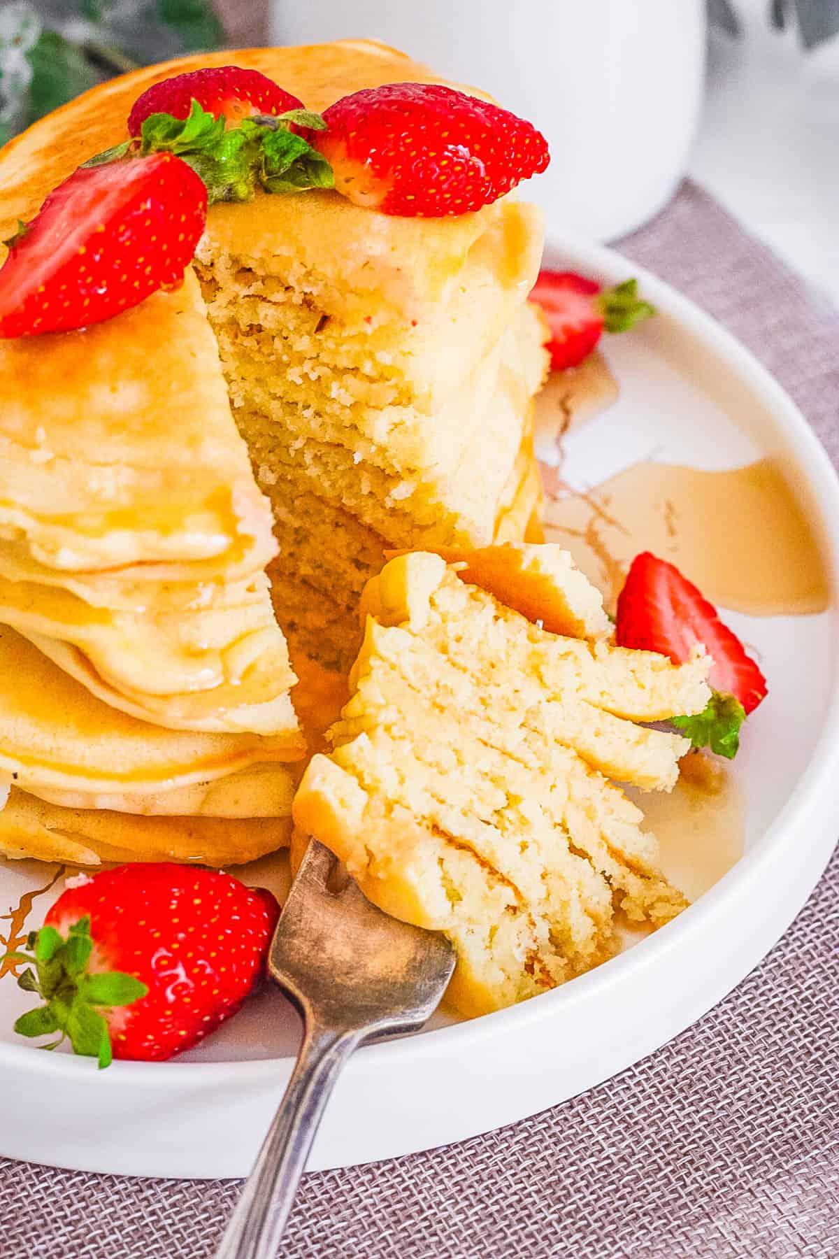 A stack of fluffy almond milk pancakes on a white plate with a forkful taken out of it.