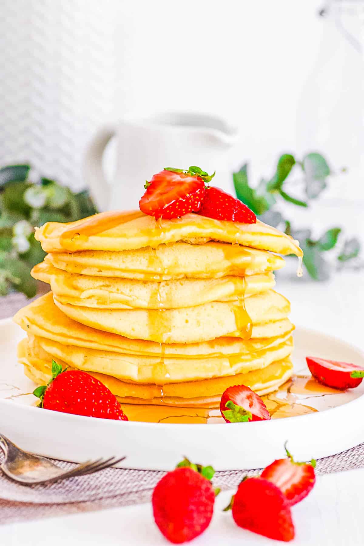 A tall stack of almond milk pancakes drizzled with maple syrup on a white plate.