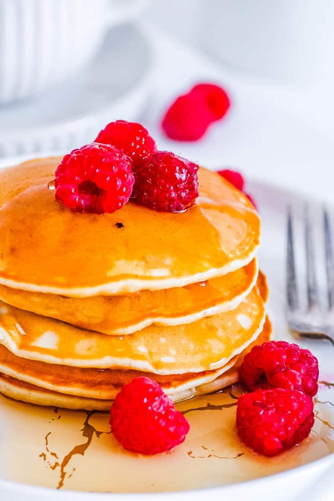 oat milk pancakes stacked on a white plate with raspberries