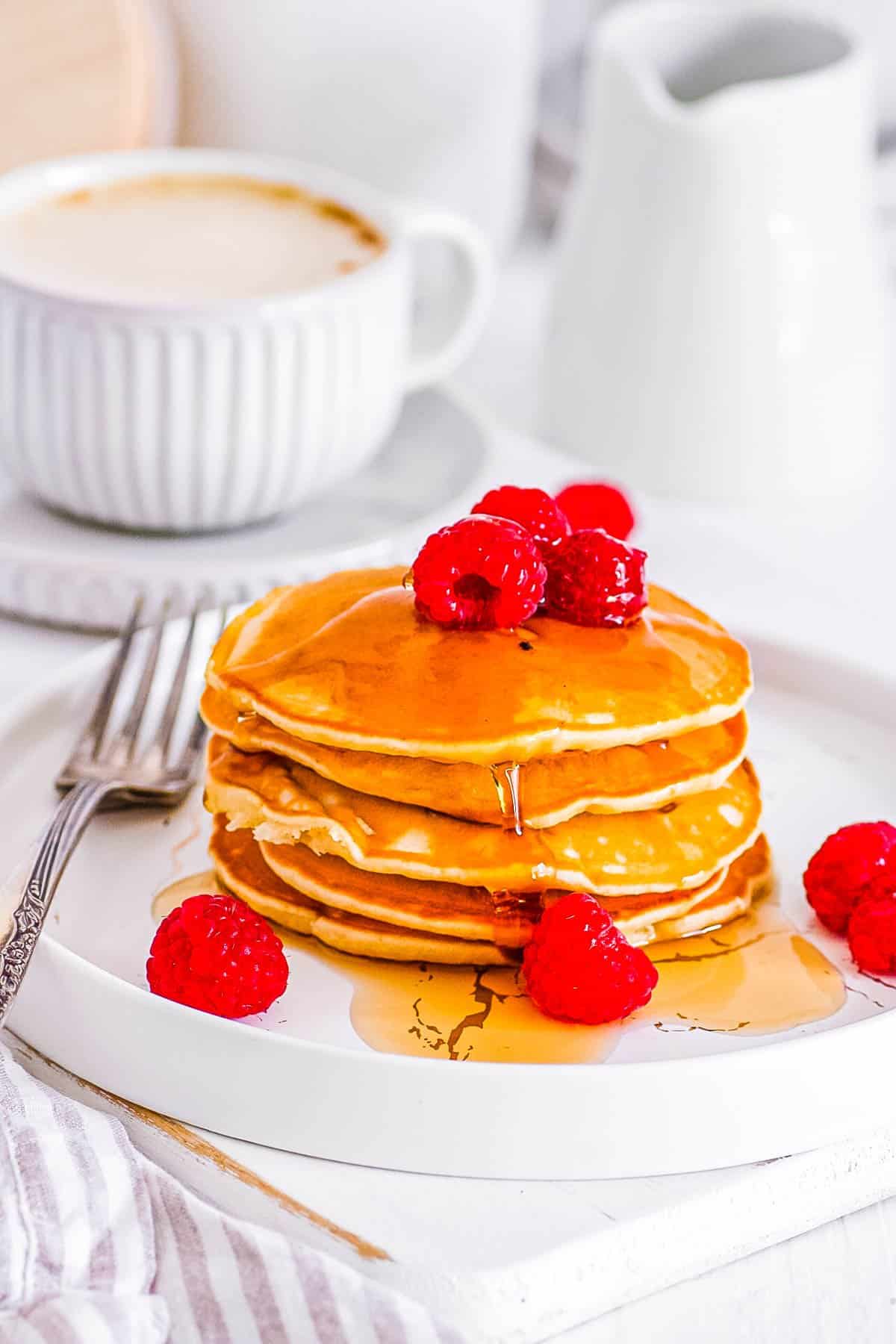 vegan oat milk pancakes stacked on a white plate with raspberries