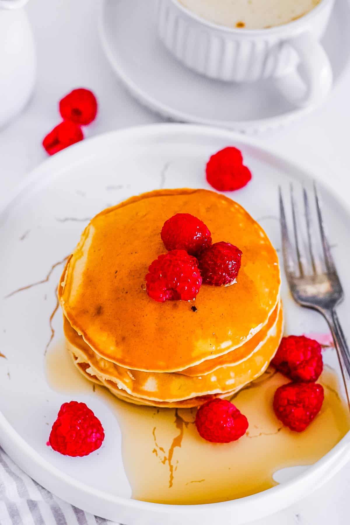 easy oat milk pancakes stacked on a white plate with raspberries