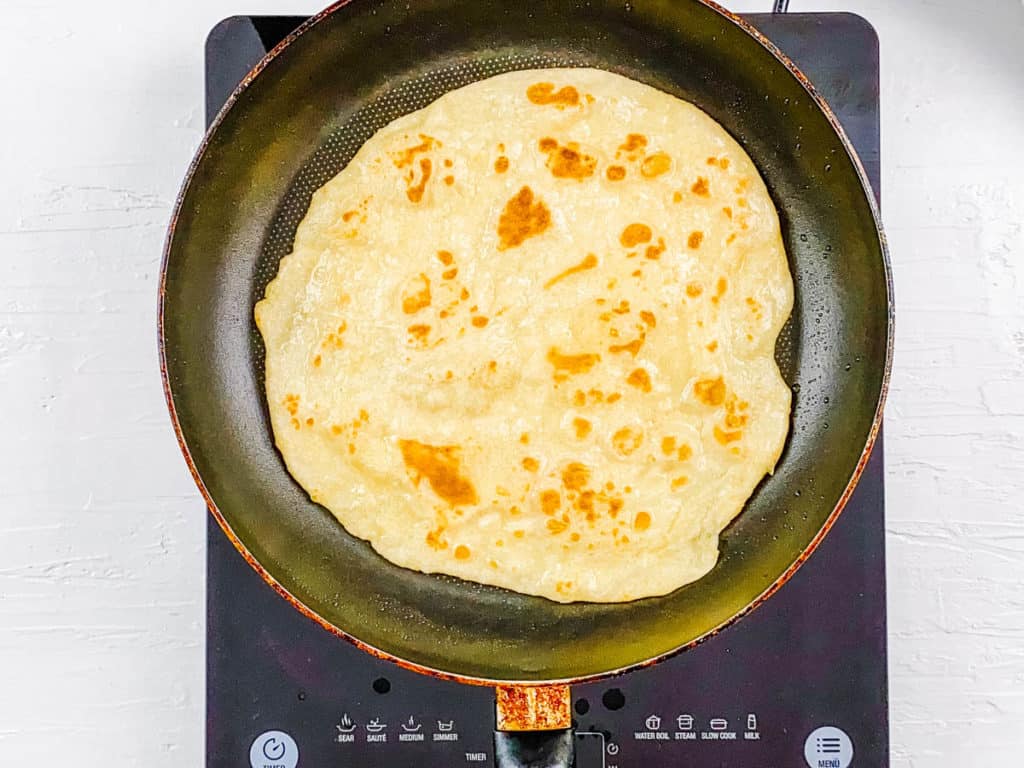 paratha dough in a skillet - roti being cooked