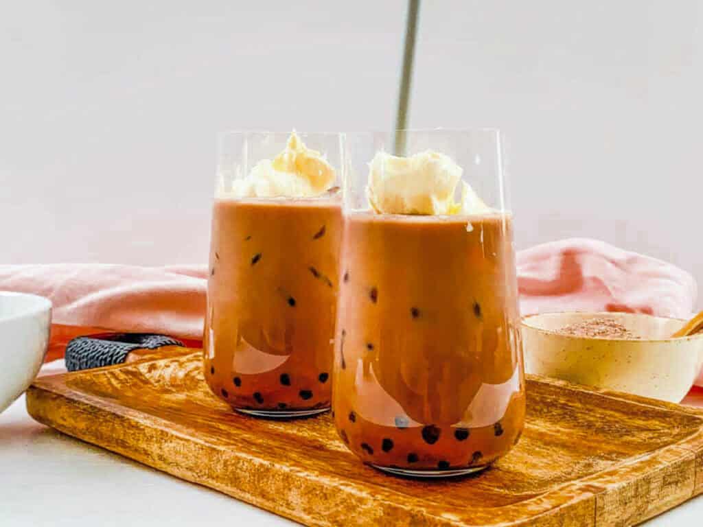 Chocolate bubble tea served in two glasses topped with whipped cream.