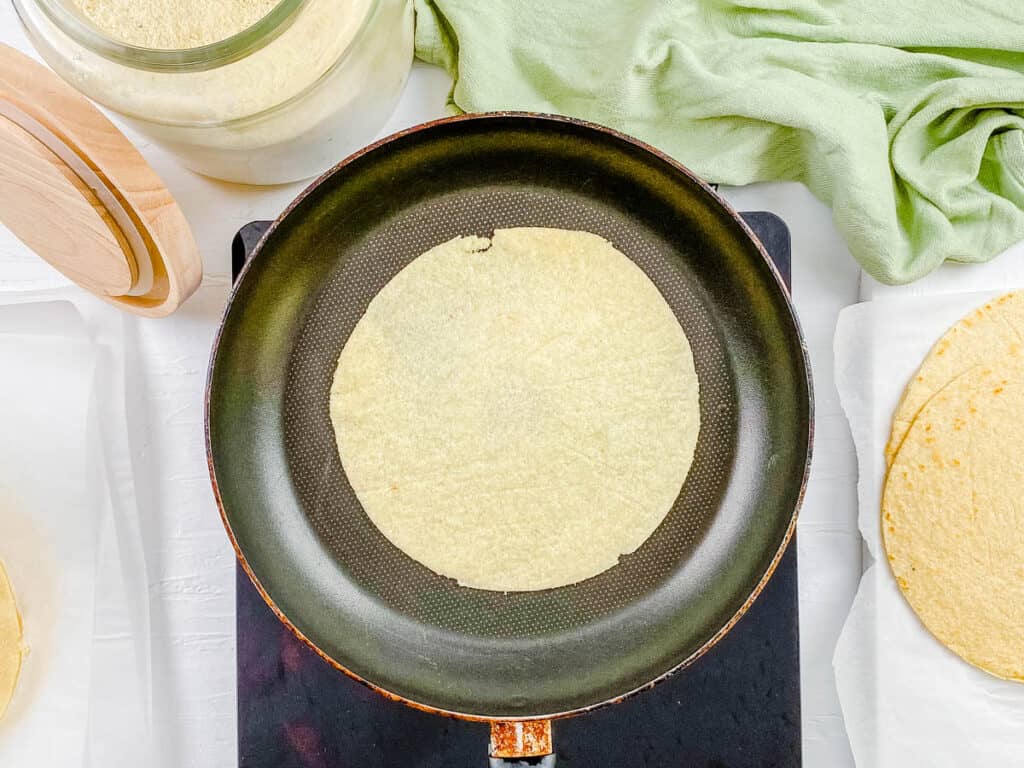 Uncooked gluten free tortilla cooking in a pan.