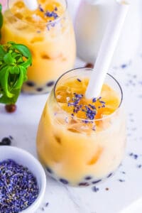 Lavender milk tea with boba in a glass with a straw.