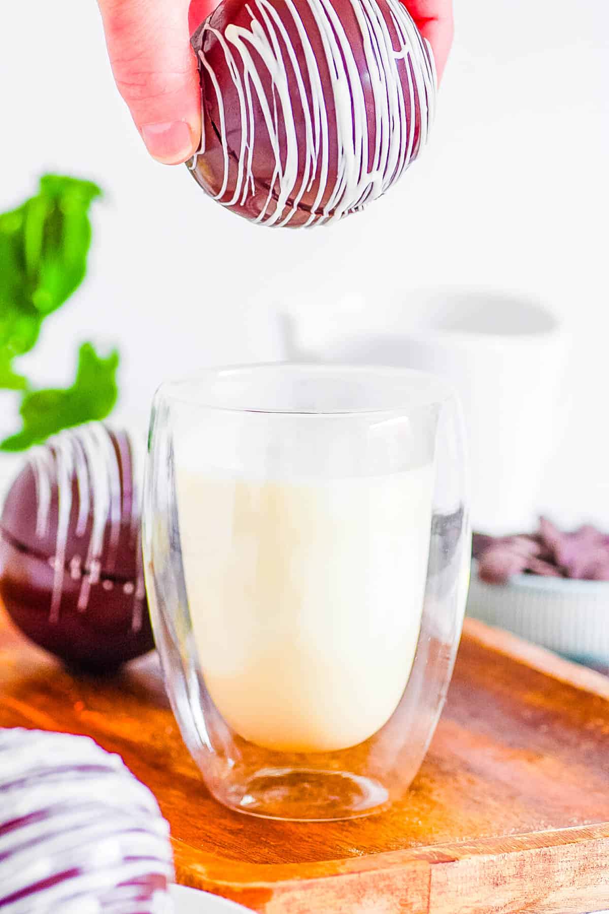 Baileys hot chocolate bomb about to be dunked into a glass of milk.