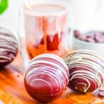 Baileys hot chocolate bombs on a wooden cutting board in front of chocolate milk.