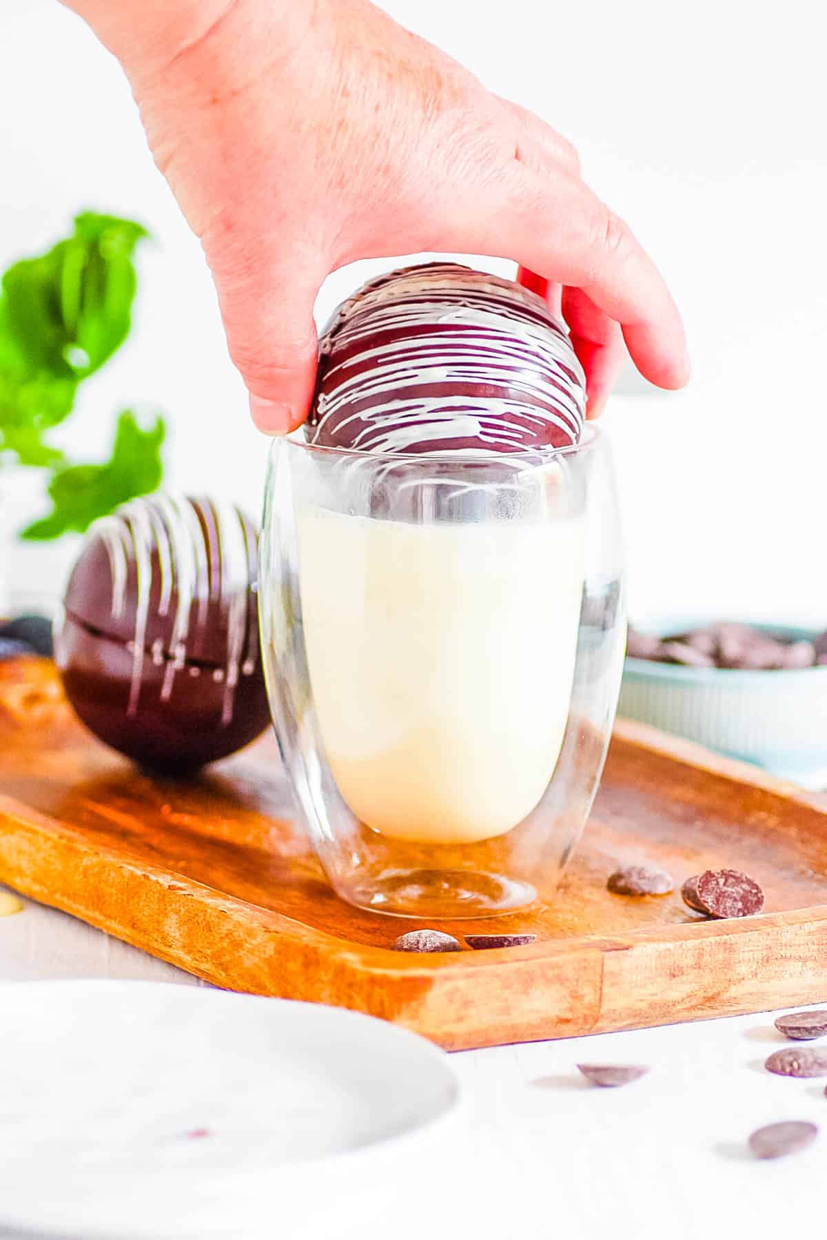 Baileys hot chocolate bomb about to be dunked into a glass of milk.