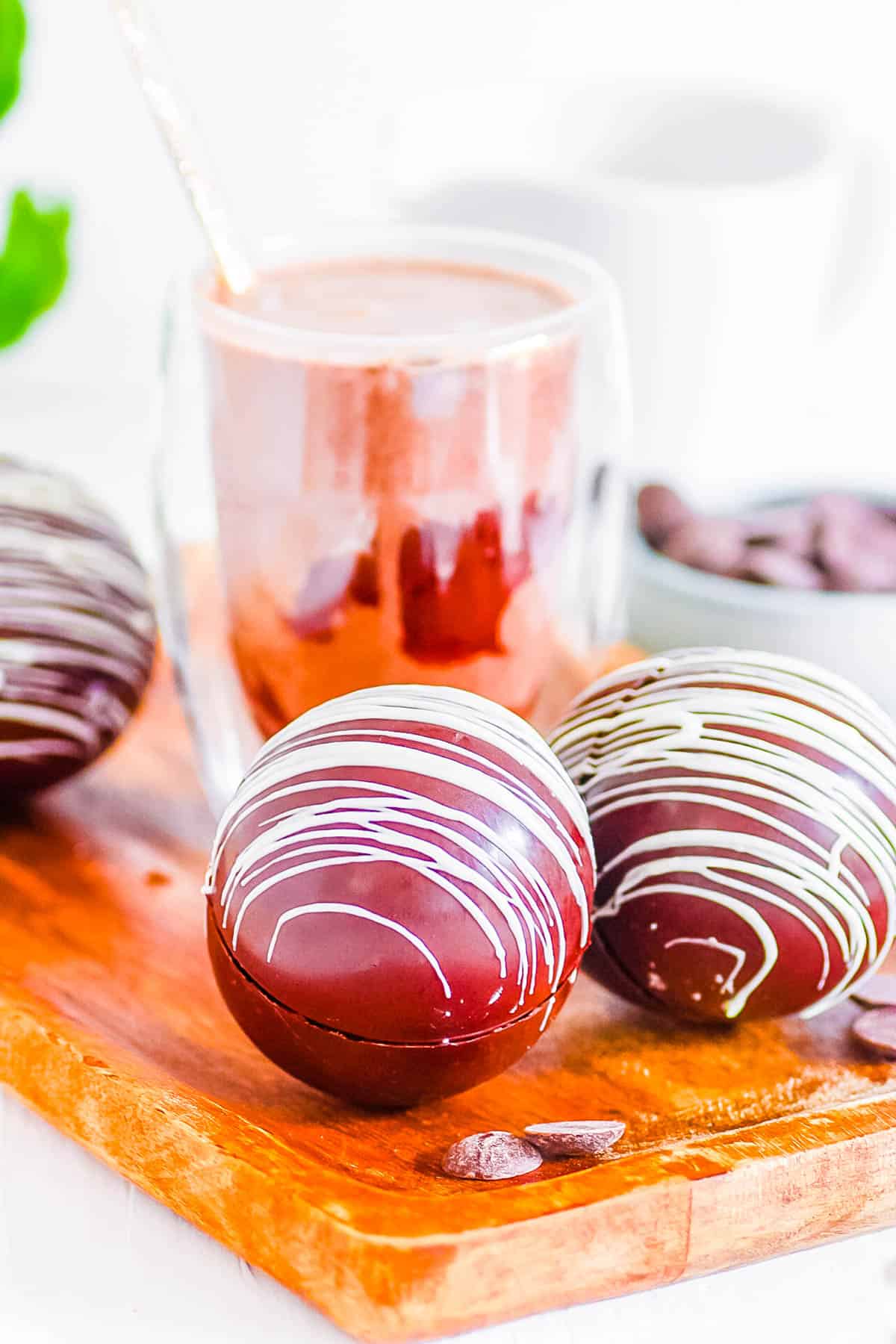 Baileys hot chocolate bombs on a wooden cutting board in front of chocolate milk.