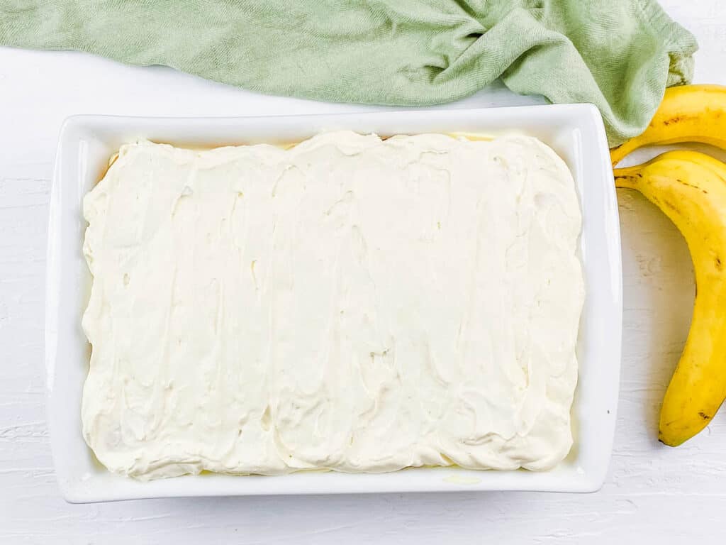 Cream cheese layer on top of bananas and Nilla wafers in a baking dish.