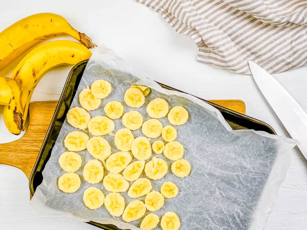 Frozen banana slices on a baking sheet with parchment paper.