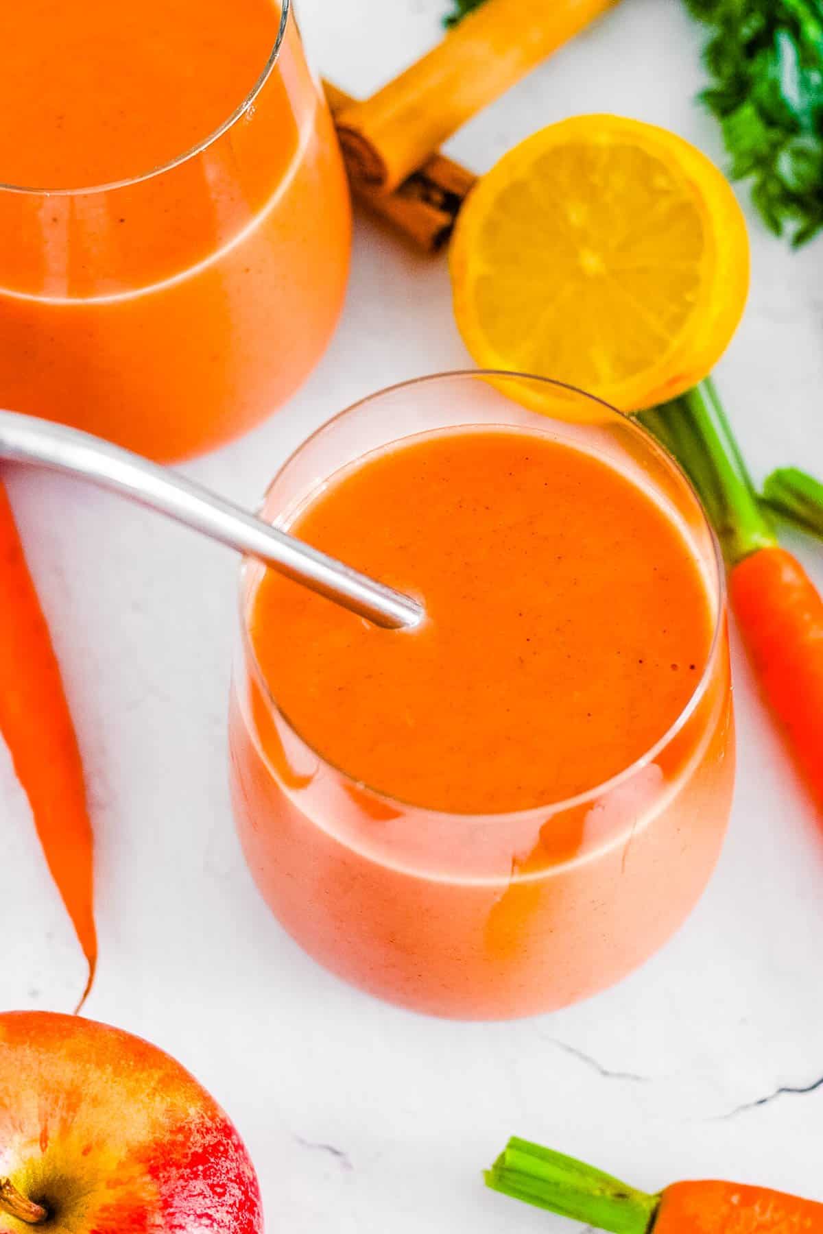 Healthy carrot apple smoothie in a glass with a straw.