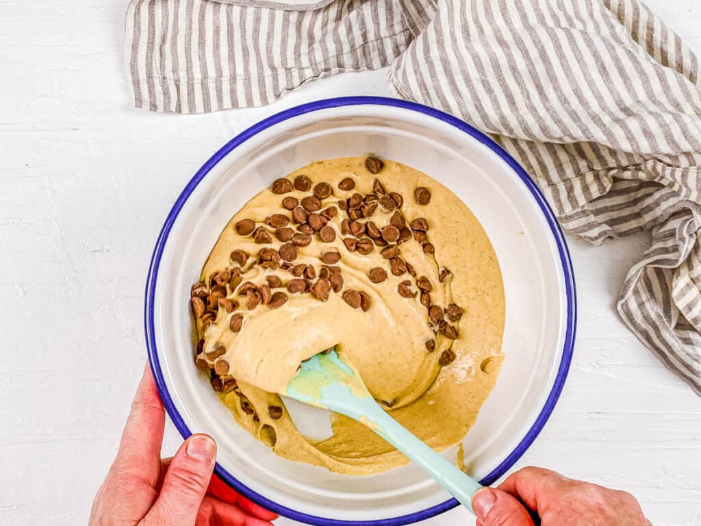 Vegan chocolate chips added to vegan pancake batter in a mixing bowl.