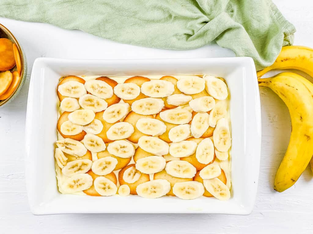 Layers of cheesecake filling, Nilla wafers and sliced bananas in a baking dish.